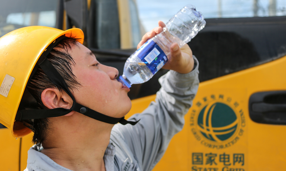 7月19日，安徽黃山供電公司帶電作業班的隊員們冒著高溫，更換線路絕緣子。圖為工作結束后，大汗淋漓的供電員工喝水解渴。（黃駿 攝）