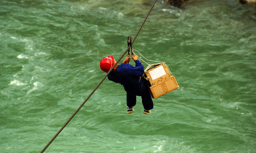 2007年，中國移動在獨龍江鄉開展“村通工程”，實現“村村通電話”。圖為移動員工用溜索運送建站物資。