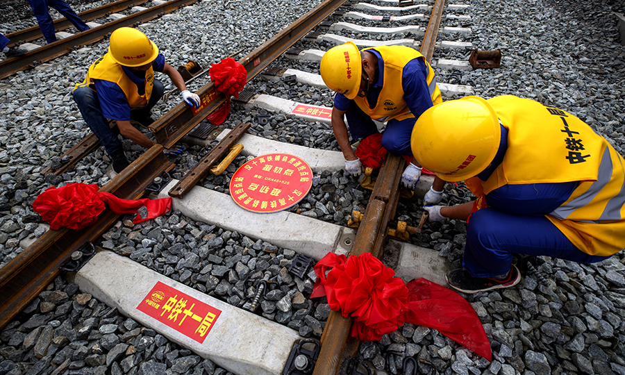 6月22日10時16分，在十堰北站余家山隧道出口，漢十高鐵最后一根長鋼軌在中國鐵建所屬中鐵十一局三公司WZ500型鋪軌機的推送下，精準地落在十堰北站有砟道床的軌枕上，精調之后，軌距誤差在正負1毫米之內。在歷時8個月鋪軌后，我國中西部客運專線的重要組成部分——武漢至十堰高鐵實現全線軌道貫通。圖為作業人員安裝夾板。（彭特 攝）