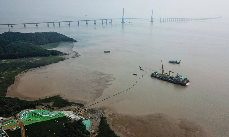 圖為6月2日，最后一段海底電纜從海纜施工船上緩緩拖向舟山大鵬山島的終端站，遠處是舟山跨海大橋。（新華社記者 徐昱 攝）