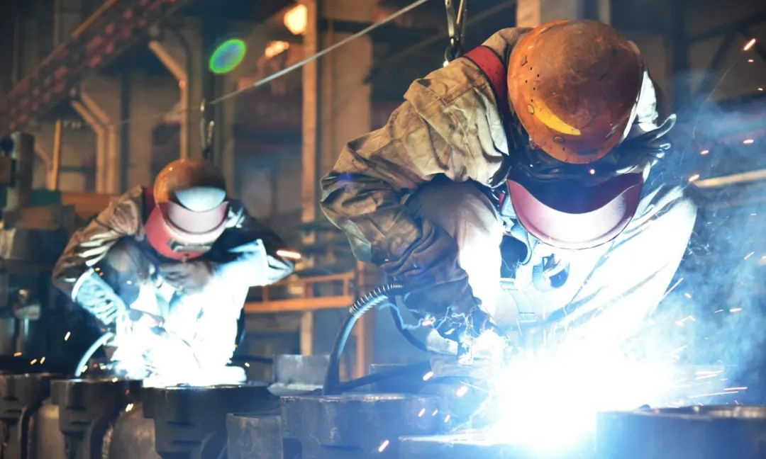 在一機集團裝焊車間生產一線，工作人員手握焊槍和焊帽在車體頂部進行高處焊接作業。