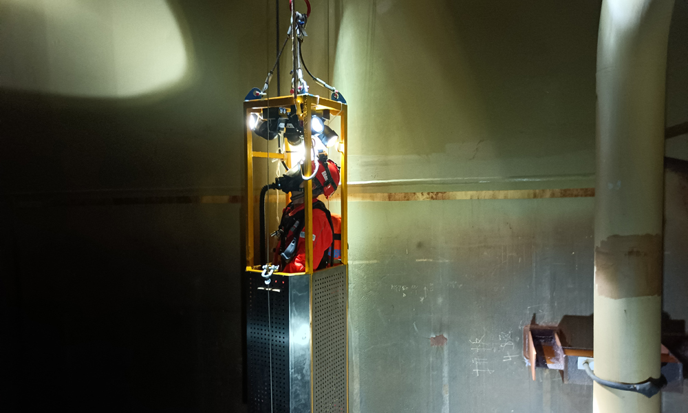 為了確保平臺凝析油艙處于良好運行狀態，掌握艙內設備運轉情況，平臺工作人員會定期開展清艙檢測作業。圖為“深海一號”現場作業人員搭乘空間極其狹小的特制工作吊籃進入凝析油艙內部進行檢查。周宇 攝