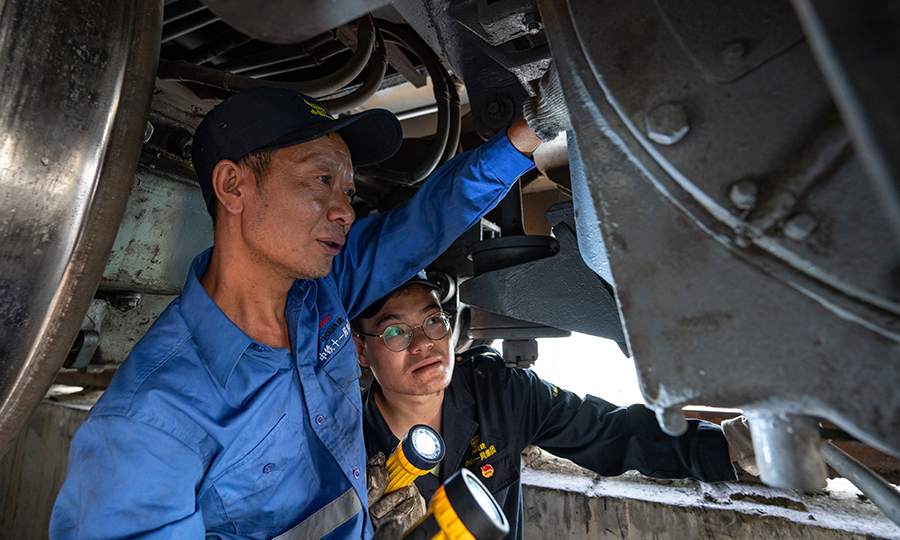 中鐵十一局集團作為拉林鐵路唯一的鋪架單位，承擔著全線的鋪軌任務，10余臺大型運輸設備晝夜不息的奔波在各個工點上，高強度的運輸作業，維保任務成了重中之重，檢修班組通過利用火車空車回基地裝卸貨的間隙，進行全面維保作業，自上場以來該班組已經維保800余車次，排除安全隱患50余次，期間未發生過1起運輸安全事故。圖為師傅帶徒弟檢查電機是否有拉傷。（丁慶濱 攝）